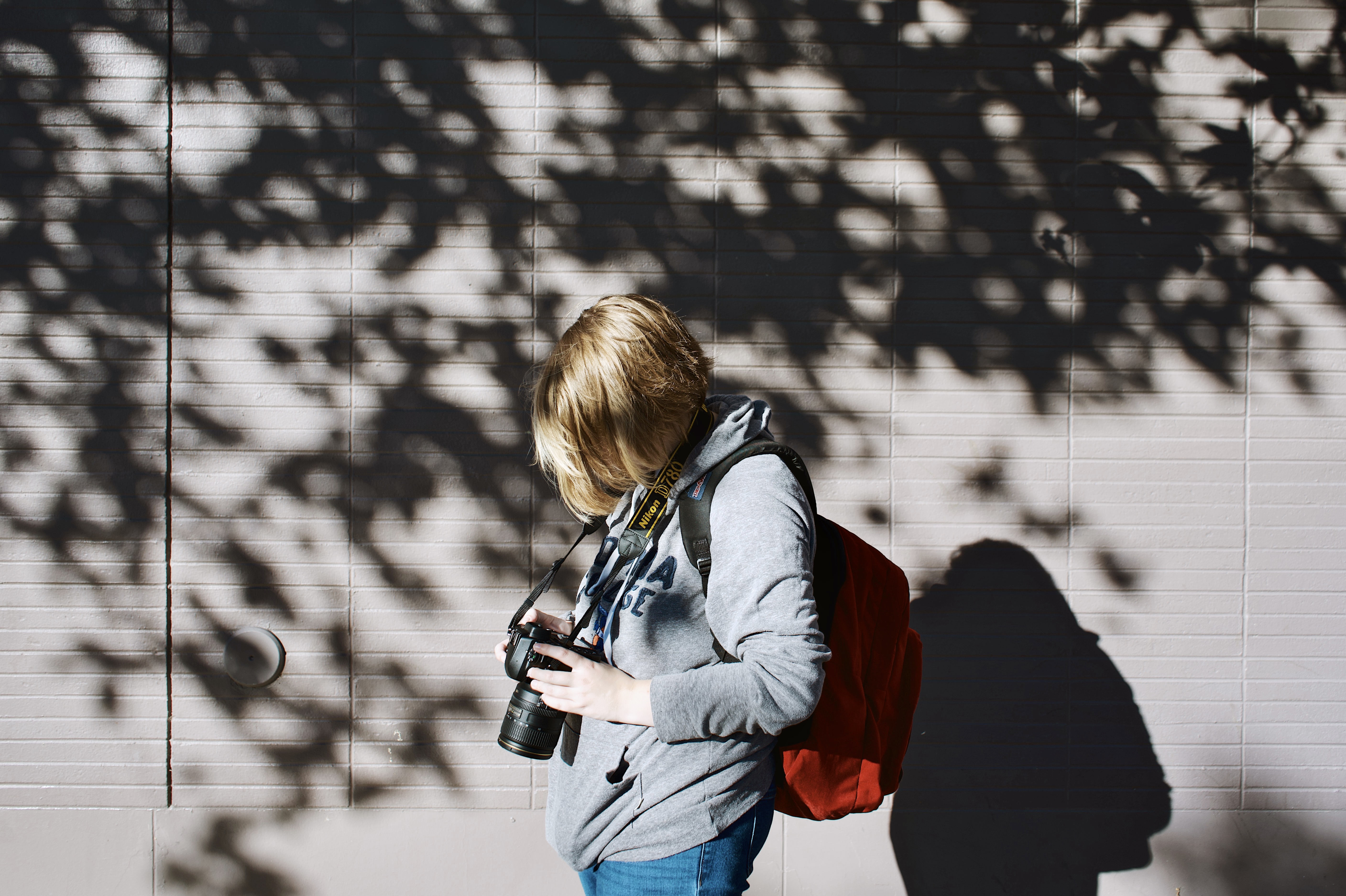 Image of Sophie, an blonde, short-haired woman, standing in front of a wall illuminated with sunlight